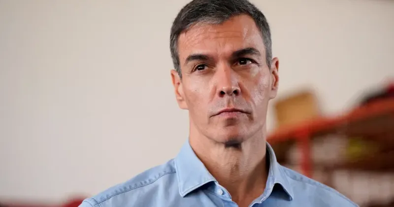 Retrato de un hombre con camisa azul claro, serio, con un taller al fondo.